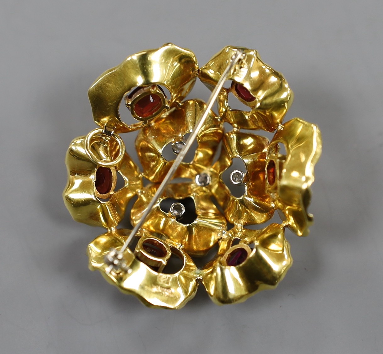 A 1960's textured 18ct gold, garnet and diamond cluster set open work flower head brooch, maker C.V.E over W., London, 1966, 44mm, gross weight, 19.2 grams.